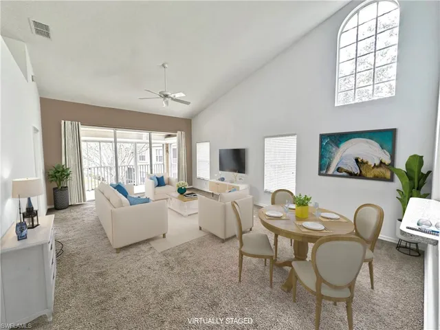 Living room with ceiling fan, high vaulted ceiling, and light carpet