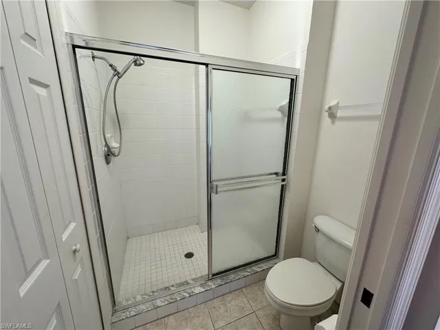 Bathroom with tile patterned floors, toilet, and a glass & tile shower with door