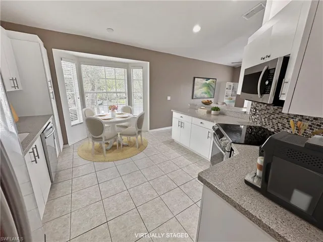 Kitchen with appliances with stainless steel finishes, light stone counters, backsplash, light tile patterned floors, and white cabinetry
