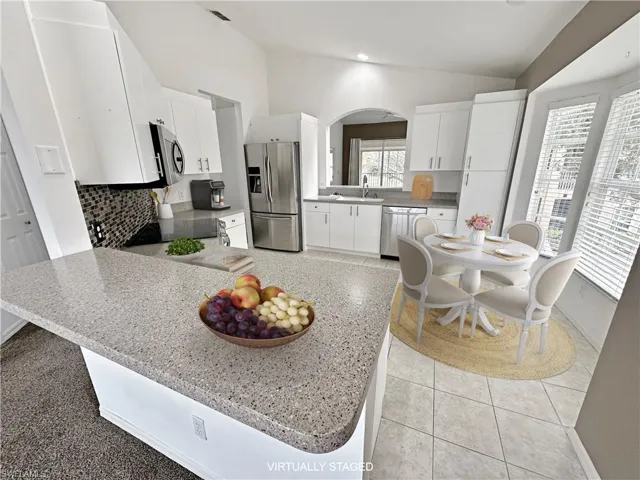 Kitchen with white cabinetry, lofted ceiling, sink, backsplash, and appliances with stainless steel finishes