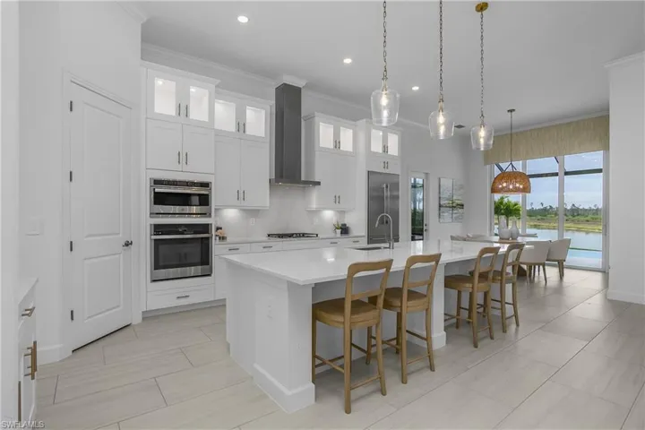 Kitchen featuring white cabinetry, crown molding, a kitchen bar, glass insert cabinets, and a kitchen island with sink