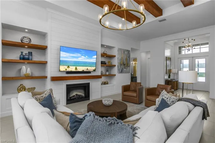 Living area featuring hanging lights, built in shelves, a fireplace, ornamental molding, and beamed ceiling