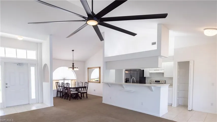 View from sliding doors: Kitchen with fridge with ice dispenser, high vaulted ceiling, range with electric cooktop, a breakfast bar, and white cabinets. Dining area, and breakfast nook.