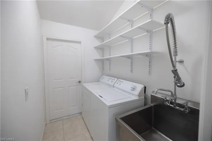 Laundry area featuring separate washer, dryer, laundry shelving, and stainless steel commercial grade sink.