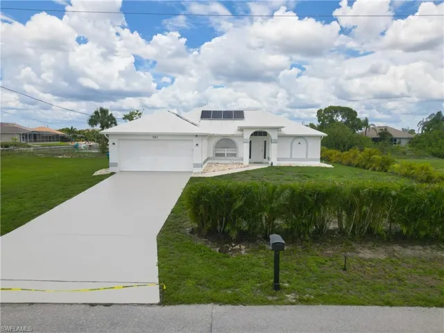 View of front of property with a front lawn, solar panels, an attached garage, and concrete driveway