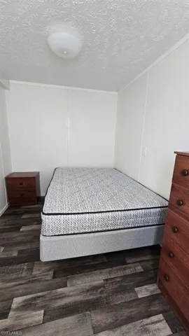 Bedroom featuring a textured ceiling, crown molding, and dark wood-style flooring