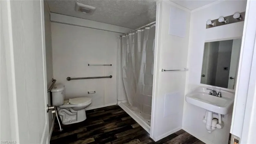 Full bath with a textured ceiling, a stall shower, and dark wood finished floors