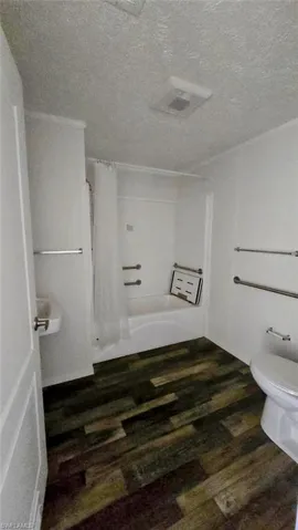 Bathroom with dark wood-type flooring, shower / bath combo, and a textured ceiling
