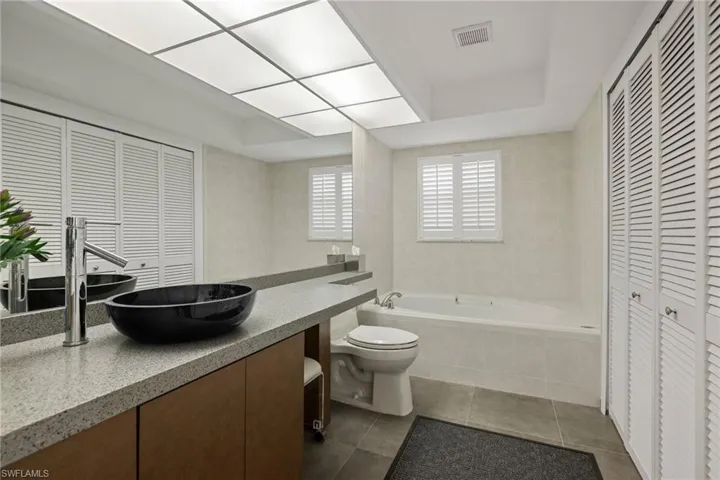 Bathroom with tile walls, tile patterned flooring, vanity, toilet, and tiled tub