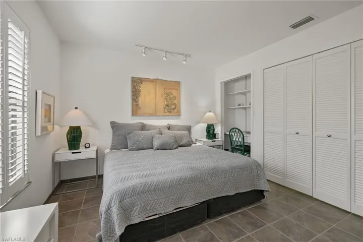 Bedroom with multiple windows, track lighting, dark tile patterned flooring, and a closet