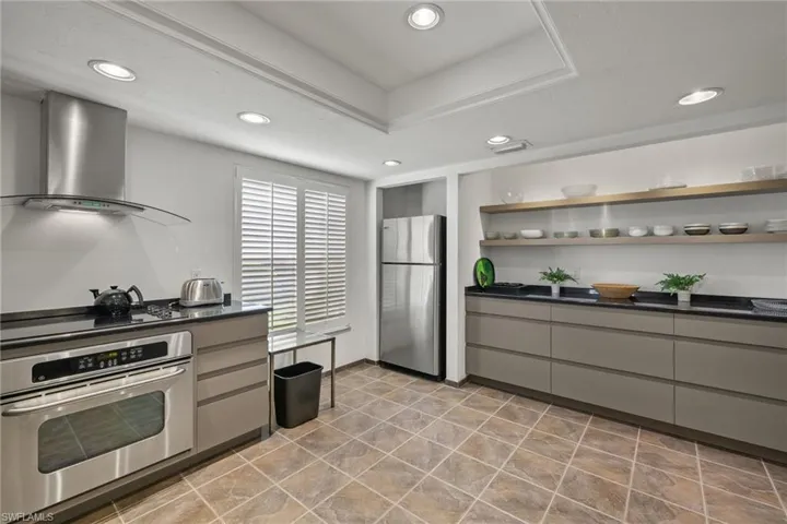 Kitchen featuring a tray ceiling, gray cabinets, wall chimney exhaust hood, and appliances with stainless steel finishes