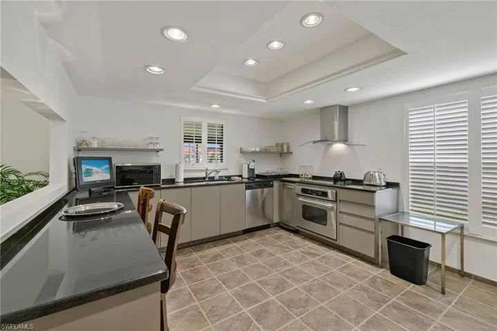 Kitchen featuring gray cabinets, appliances with stainless steel finishes, sink, a tray ceiling, and wall chimney exhaust hood