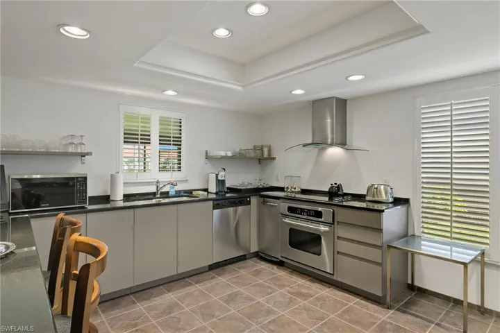 Kitchen featuring sink, gray cabinetry, black appliances, a raised ceiling, and wall chimney range hood