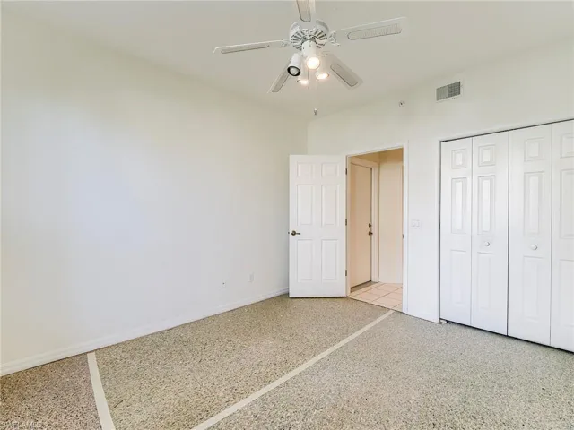 Unfurnished bedroom with speckle patterned floor, a closet, and a ceiling fan