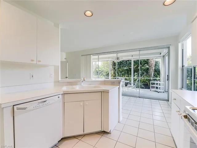 Kitchen with white appliances, white cabinetry, a peninsula, light countertops, and light tile patterned flooring