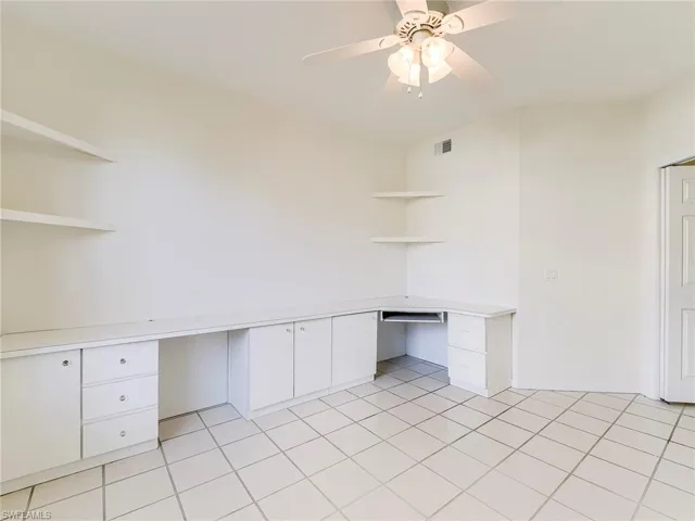 Unfurnished office featuring built in study area, ceiling fan, and light tile patterned floors
