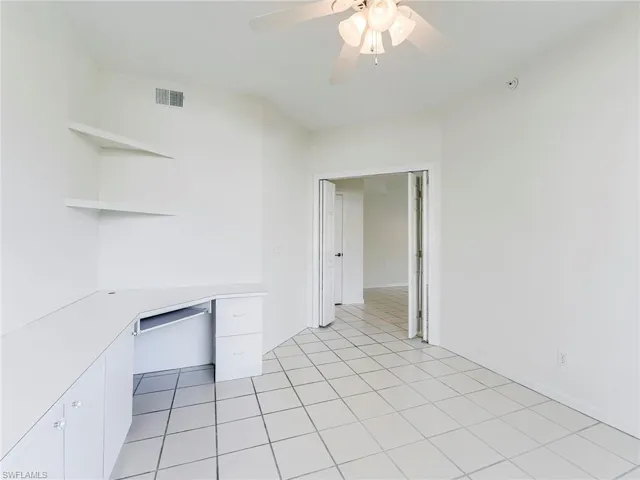 Unfurnished office featuring a ceiling fan, built in desk, and light tile patterned floors