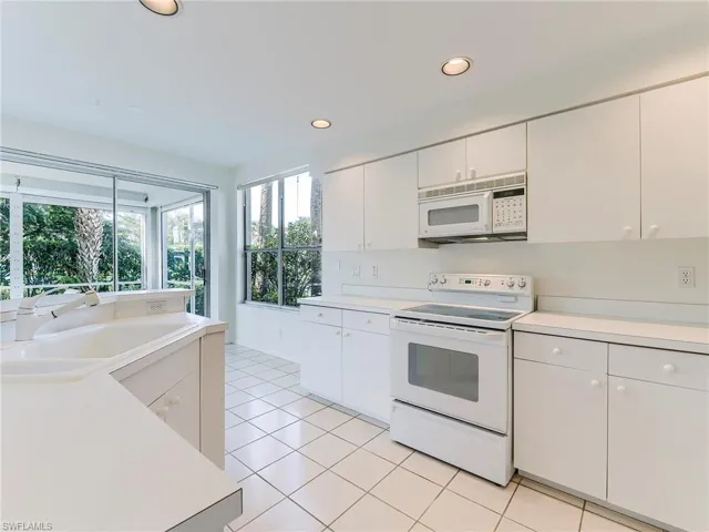 Kitchen with white appliances, light countertops, white cabinets, and recessed lighting