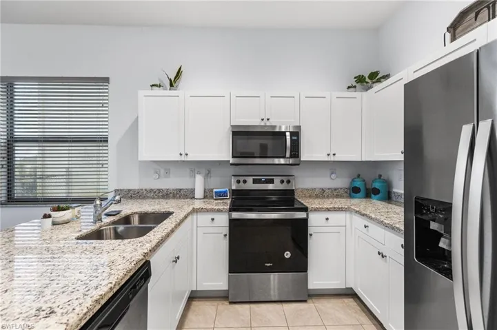 Kitchen featuring white cabinetry, sink, light tile patterned floors, stainless steel appliances, and light stone countertops