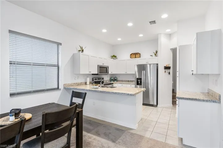 Kitchen featuring light tile patterned flooring, white cabinetry, kitchen peninsula, stainless steel appliances, and light stone countertops
