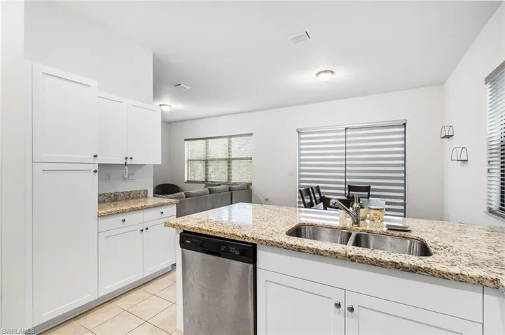 Kitchen featuring sink, white cabinetry, light stone counters, light tile patterned floors, and dishwasher