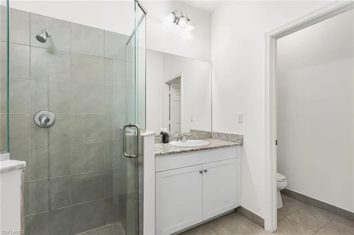 Bathroom featuring vanity, toilet, an enclosed shower, and tile patterned flooring