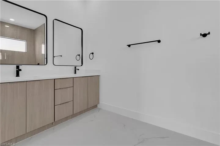 Bathroom with double vanity and light marble finish flooring