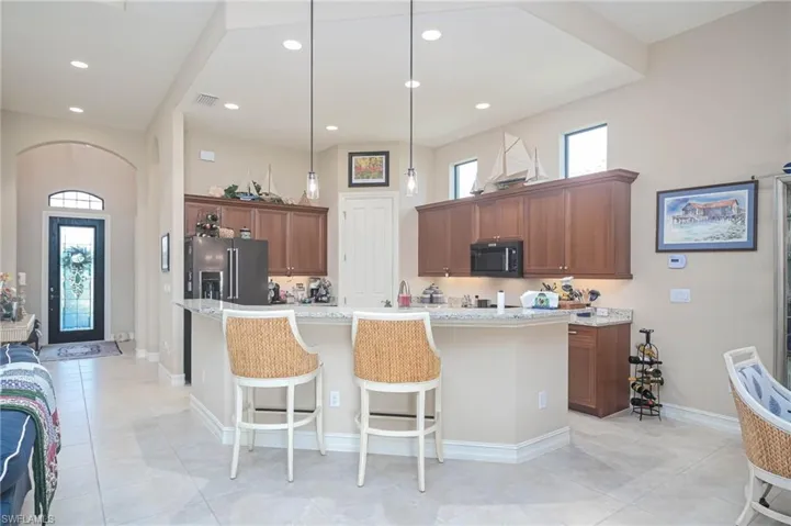 Kitchen featuring an island with sink, pendant lighting, light stone countertops, and stainless steel fridge with ice dispenser