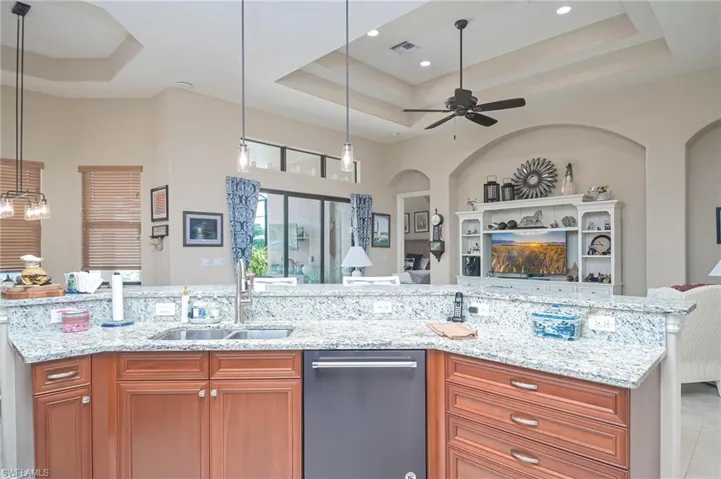 Kitchen with ceiling fan, decorative light fixtures, a tray ceiling, and light stone counters
