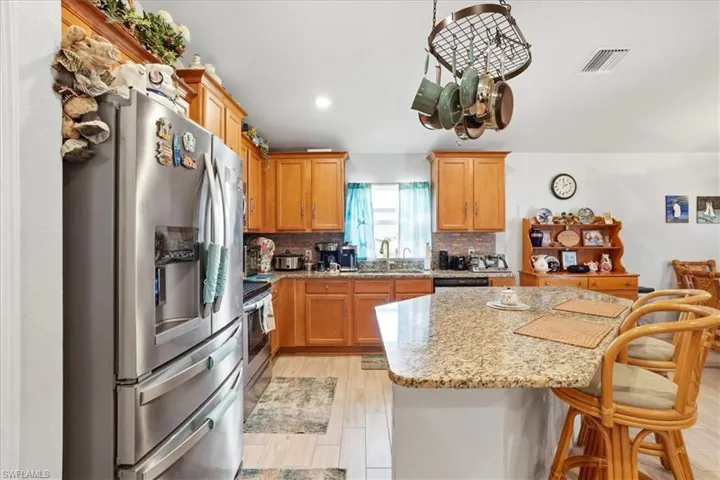 Kitchen with stainless steel appliances, light stone counters, a breakfast bar, tasteful backsplash, and a center island