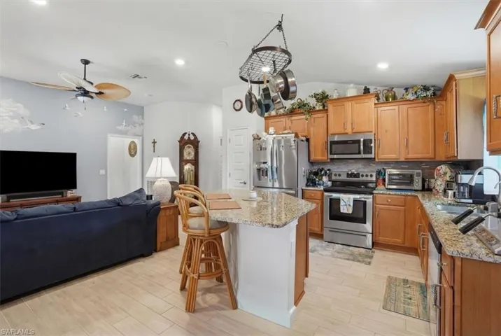 Kitchen featuring open floor plan, light stone counters, a kitchen bar, stainless steel appliances, and backsplash