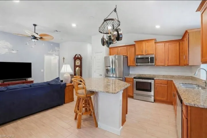 VIRTUALLY STAGED Kitchen with open floor plan, a kitchen breakfast bar, stainless steel appliances, light stone countertops, and light wood finished floors
