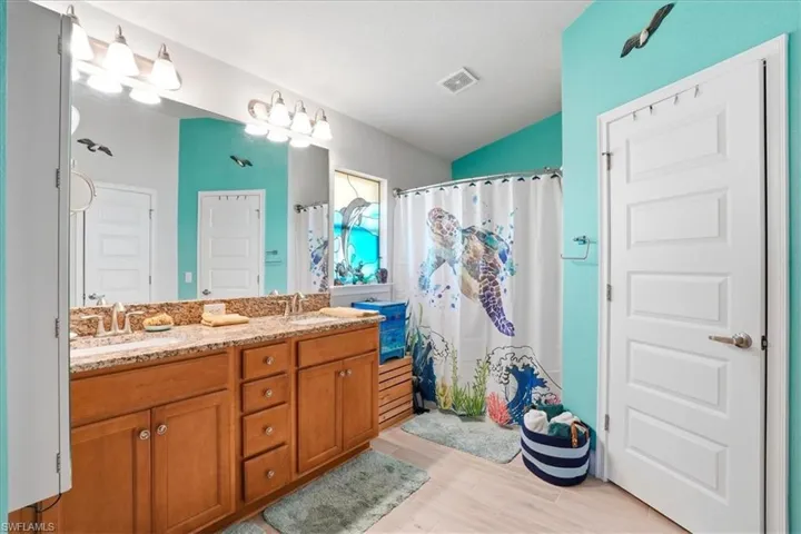 Bathroom with double vanity, a shower with shower curtain, light wood-style flooring, and vaulted ceiling