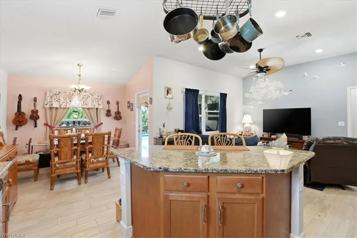 Kitchen with light wood finished floors, open floor plan, light stone counters, wood finish cabinetry, and a kitchen island
