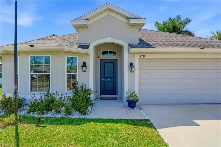 Doorway to property with an attached garage, roof with shingles, concrete driveway, stucco siding, and a lawn