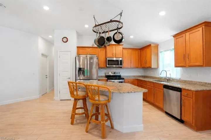 VIRTUALLY STAGED Kitchen with a kitchen breakfast bar, stainless steel appliances, light stone counters, light wood-style flooring, and lofted ceiling