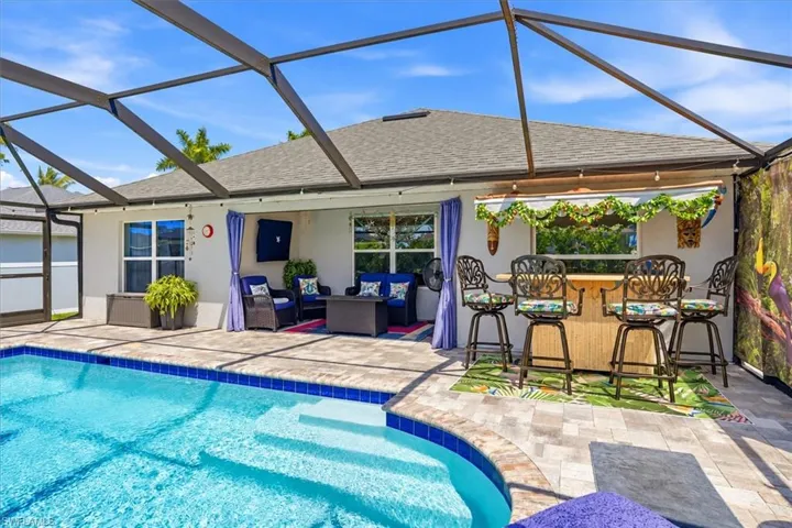 Screened outdoor living area with a built-in pool, textured patio, and a dedicated bar space