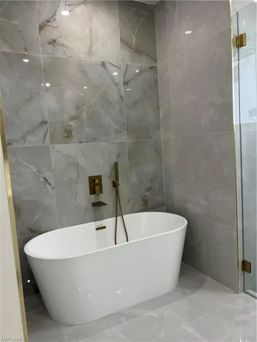 Full bathroom with tile walls, marble look tile flooring, and a freestanding bath