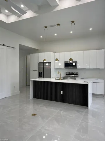 Kitchen featuring range, fridge, modern cabinets, a spacious island, and light marble finish floors