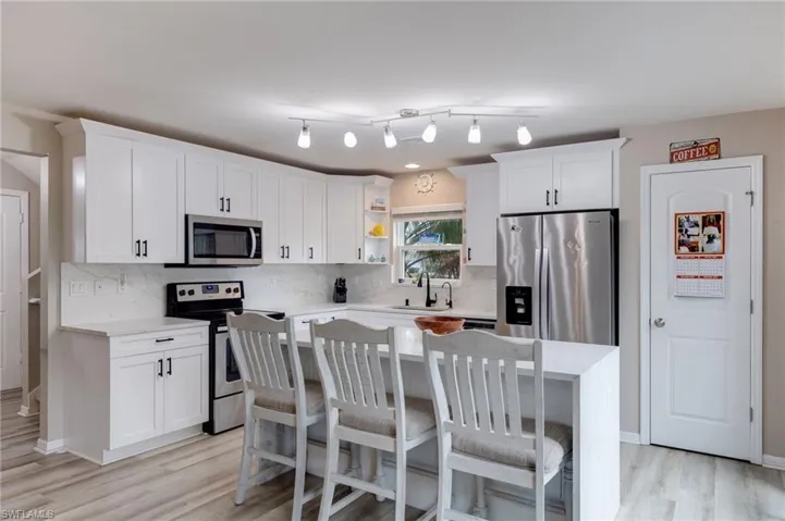 Kitchen featuring stainless steel appliances, a kitchen breakfast bar, tasteful backsplash, white cabinetry, and light stone countertops