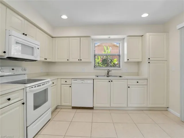 Kitchen with light tile patterned flooring, white appliances, sink, and white cabinets