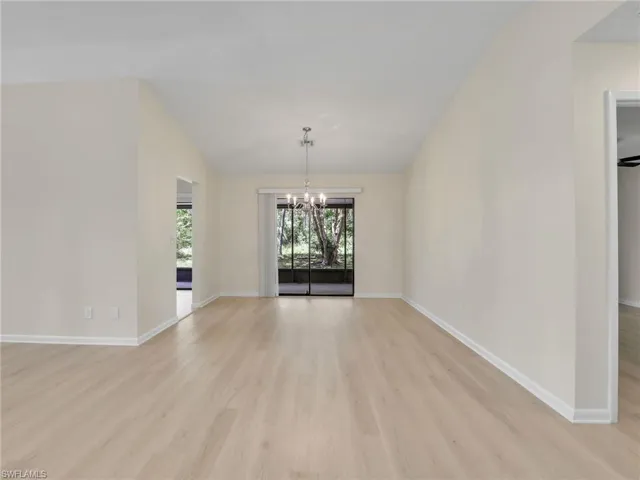 Spare room featuring an inviting chandelier, lofted ceiling, and light wood-type flooring