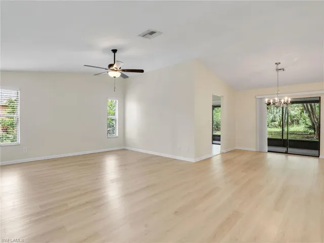 Unfurnished room with ceiling fan with notable chandelier, light hardwood / wood-style flooring, and vaulted ceiling
