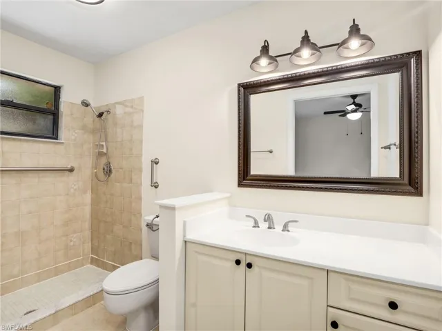 Bathroom with tiled shower, vanity, ceiling fan, and toilet