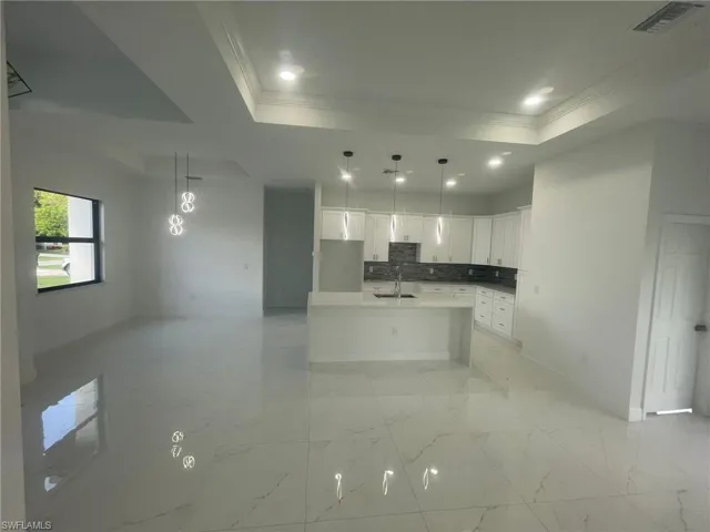 Kitchen with decorative backsplash, white cabinetry, a center island with sink, and light tile patterned floors