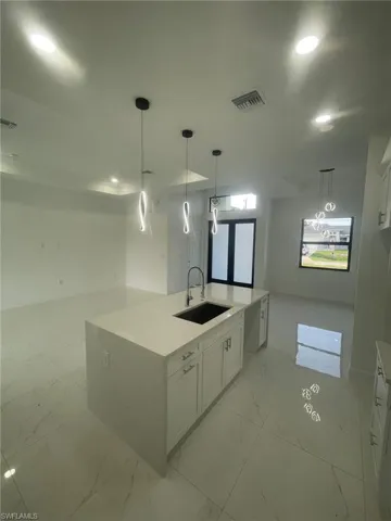 Kitchen with light tile patterned floors, white cabinetry, sink, and pendant lighting