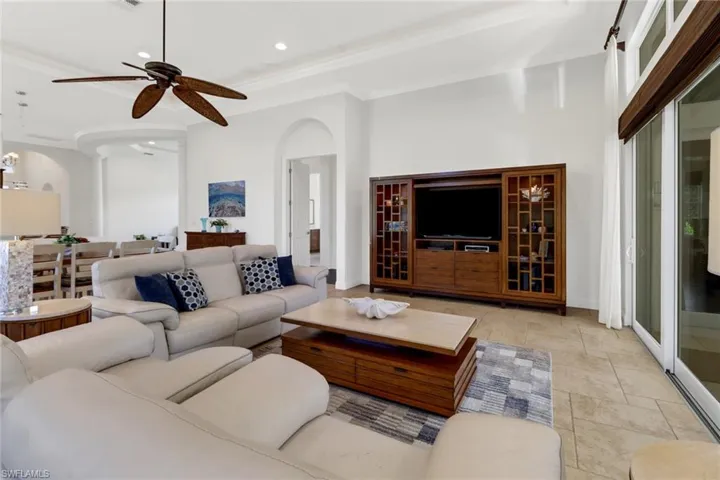 Living room with a towering ceiling, crown molding, light tile patterned flooring, and ceiling fan
