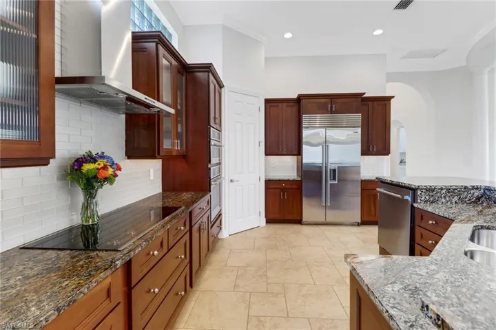 Kitchen featuring wall chimney range hood, ornamental molding, stainless steel appliances, and light stone counters