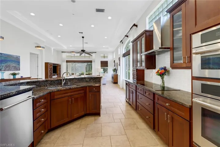 Kitchen featuring backsplash, dark stone counters, stainless steel appliances, wall chimney exhaust hood, and sink
