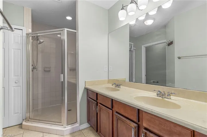 Bathroom with double vanity, a shower stall, and light tile patterned floors